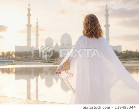 Travel to the United Arab Emirates, Abu Dhabi. Woman in white Arabic dress looking at Sheikh Zayed Great white mosque. famous Abu Dhabi sightseeing. Travel to the United Arab Emirates, Abu Dhabi. Woman in white Arabic dress looking at Sheikh Zayed Great white mosque. famous Abu Dhabi sightseeing. 119485344