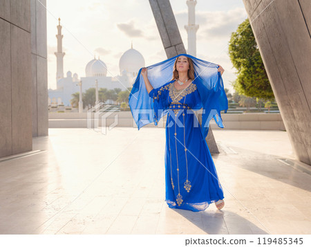 Travel to the United Arab Emirates, Abu Dhabi. Woman in blue Arabic dress near Sheikh Zayed Great white mosque. famous Abu Dhabi sightseeing. 119485345