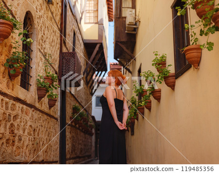 Young woman in elegant black dress walking in cozy old town Keleci, Antalya, Turkey during summer day. female traveler discover interesting places and popular attractions Young woman in elegant black dress walking in cozy old town Keleci, Antalya, Turkey during summer day. female traveler discover interesting places and popular attractions 119485356
