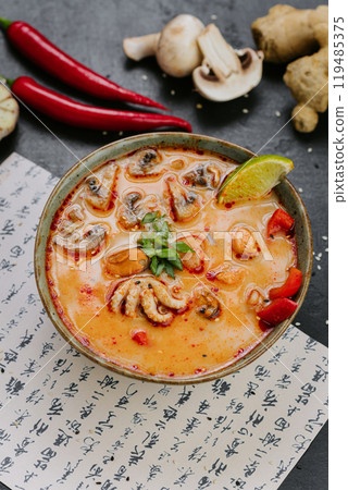 Spicy Tom Yum soup with seafood, mushrooms, and chili served with lime and herbs in Asian style Spicy Tom Yum soup with seafood, mushrooms, and chili served with lime and herbs in Asian style 119485375