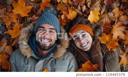 Autumn or fall season. A couple laying on the ground with their hands in the air, smiling and looking at the camera while surrounded by autumn leaves. 119485379