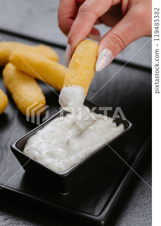 Dipping crispy cheese stick into creamy sauce. Perfect snack for cheese lovers and party appetizers Dipping crispy cheese stick into creamy sauce. Perfect snack for cheese lovers and party appetizers 119485382