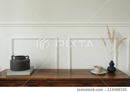 Elegant minimal interior still life. Scandinavian interior design. Black boho organic vases with dry flowers grass. Cup of tea, coffee. Empty white wall background. Modern living room design trend. 119486585