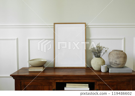 Elegant sideboard arrangement. Mahogany sideboard cabinet. Blank vertical wooden picture mock up poster frame. Clay vases, dry flowers, books, candle. Modern interior design, white wall background. Elegant sideboard arrangement. Mahogany sideboard cabinet. Blank vertical wooden picture mock up poster frame. Clay vases, dry flowers, books, candle. Modern interior design, white wall background. 119486602