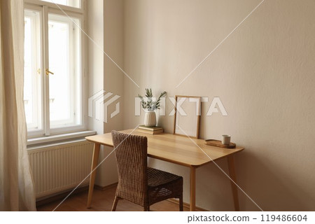 Empty vertical picture frame mockup. Wooden desk, table. Vase with olive branches, books, cup of coffee. Elegant working space, home office. Summer interior design. Beige walls. Blurred curtain window Empty vertical picture frame mockup. Wooden desk, table. Vase with olive branches, books, cup of coffee. Elegant working space, home office. Summer interior design. Beige walls. Blurred curtain window 119486604