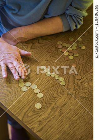 senior female sitting miserably at the table at home and counting coins. High quality photo senior female sitting miserably at the table at home and counting coins. High quality photo 119486869