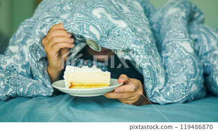 Young woman reaching hand for tasty peace of cake while lying in bed. High quality photo Young woman reaching hand for tasty peace of cake while lying in bed. High quality photo 119486870