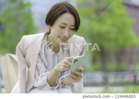 辦公區的一位女商人坐在長椅上操作智慧型手機 119486883