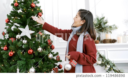 Woman hands decorate Christmas tree red ball, bauble, snow flake. Asian woman decor bauble ball christmas tree in xmas holiday winter seasonal celebration. Close up hands holding silver star decorate 119486898
