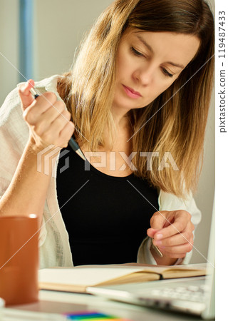 Freelance woman sitting at table using laptop and writing in notebook. Remote work at home office 119487433