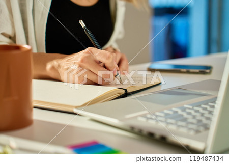 Person is sketching in notebook while working remotely at desk with laptop. Freelance work at home office. Graphic designer drawing sketch 119487434