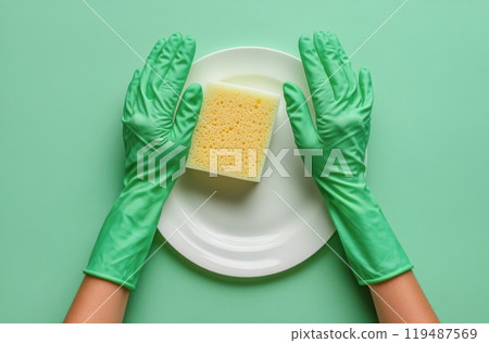 Hands in green gloves placing a bright yellow sponge on a white plate against a green background 119487569