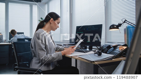 Adult, beautiful female analyst checking data in paper documents Adult, beautiful female analyst checking data in paper documents 119488907