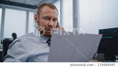 Financial specialist talks to business client by mobile phone, analyzes paper documents 119488945