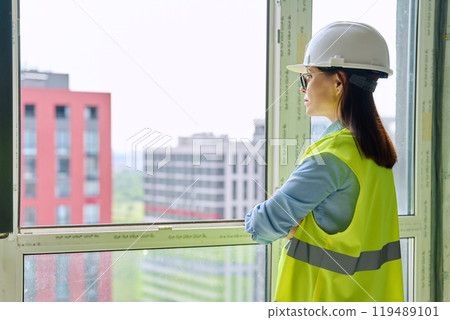 Back view of female industrial worker in protective helmet vest looking at new buildings Back view of female industrial worker in protective helmet vest looking at new buildings 119489101