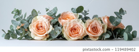 Delicate arrangement of light peach and cream roses with green eucalyptus leaves on a wooden surface 119489402