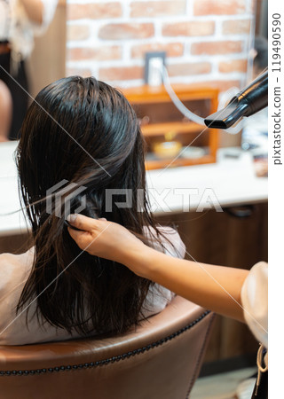 理髮師將吹風機應用於長髮女性的頭髮 119490590