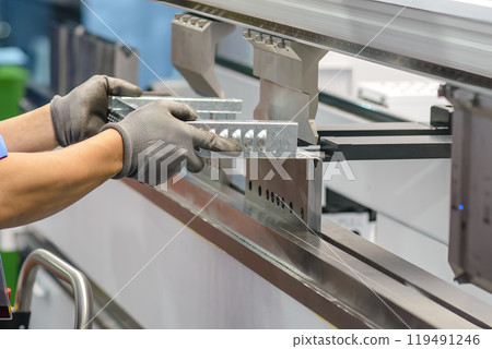 Close up the bending machine operator hold the sheet metal parts with protective glove. 119491246