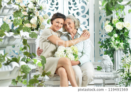 Elderly mother and daughter sitting on a bench surrounded by flowers 119491569