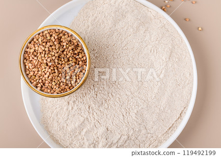 Buckwheat flour in a ceramic plate and raw buckwheat grain on a bowl on beige background, top view Buckwheat flour in a ceramic plate and raw buckwheat grain on a bowl on beige background, top view 119492199