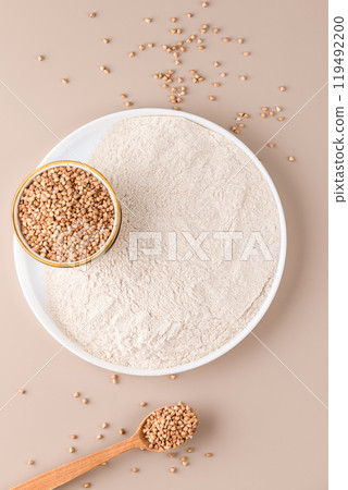 Buckwheat flour in a ceramic plate and raw buckwheat grain on a bowl on beige background, top view Buckwheat flour in a ceramic plate and raw buckwheat grain on a bowl on beige background, top view 119492200