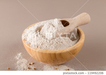 Buckwheat flour in a wooden bowl with wooden scoop on beige background 119492206