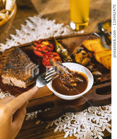 Person dipping grilled steak in sauce with beer in background Person dipping grilled steak in sauce with beer in background 119492470