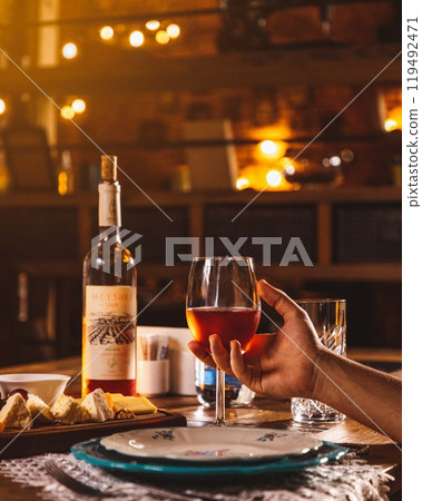 Person holding glass of wine with cheese and wine bottle on table 119492471