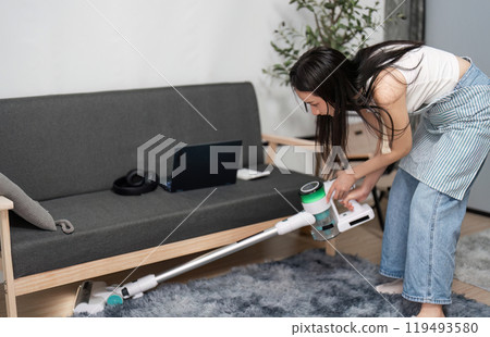 Young Woman Vacuuming and Cleaning a Modern Living Room with a Cordless Vacuum Cleaner 119493580