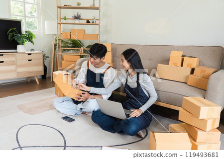 Young Couple Selling Products Online from Home, Surrounded by Cardboard Boxes and Using Laptop and Smartphone Young Couple Selling Products Online from Home, Surrounded by Cardboard Boxes and Using Laptop and Smartphone 119493681