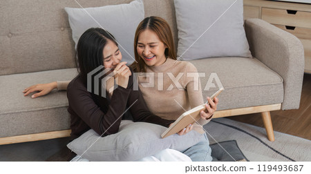 Happy Lesbian Couple Relaxing in Modern Living Room, Reading and Laughing Together on Comfortable Sofa 119493687