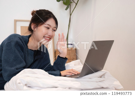 Relaxed Young Woman Using Laptop in Cozy Home Setting, Smiling and Waving, Casual Lifestyle, Remote Work or Online Communication Relaxed Young Woman Using Laptop in Cozy Home Setting, Smiling and Waving, Casual Lifestyle, Remote Work or Online Communication 119493773