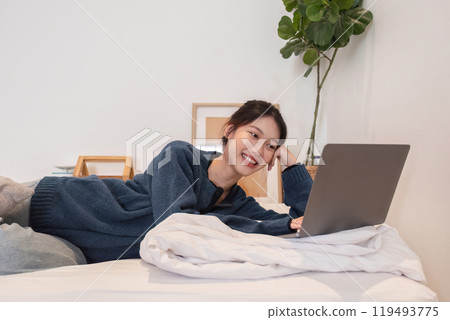 Relaxed Young Woman Using Laptop on Bed in Cozy Modern Home Interior with Green Plant and Minimalist Decor Relaxed Young Woman Using Laptop on Bed in Cozy Modern Home Interior with Green Plant and Minimalist Decor 119493775