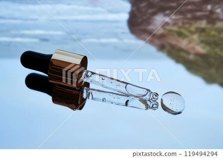 Pipette with facial serum against the background of the sea in blue tones. Pipette with facial serum against the background of the sea in blue tones. 119494294