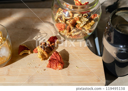 Dried broken pieces caps of the Amanita muscaria mushroom (fly agaric) lying on a cutting board, coffee grinder and a glass with ground mushroom on ice cubes in the background Dried broken pieces caps of the Amanita muscaria mushroom (fly agaric) lying on a cutting board, coffee grinder and a glass with ground mushroom on ice cubes in the background 119495138