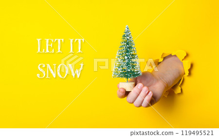 A hand holding a small Christmas tree in front of a yellow background 119495521