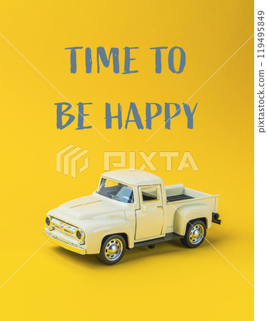 A toy truck is sitting on a yellow background with the words Time to be happy A toy truck is sitting on a yellow background with the words Time to be happy 119495849