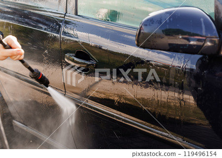 High-Pressure Water Jet Cleaning a Black Car Door on a Sunny Day 119496154