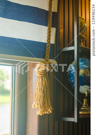 Elegant curtain with nautical rope tie-back beside a globe in marine style room. High quality photo Elegant curtain with nautical rope tie-back beside a globe in marine style room. High quality photo 119496234