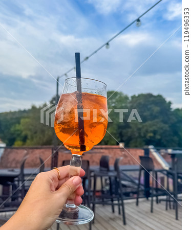 female hand with ring on finger holding the glass of Aperol spritz cocktail . High quality photo 119496353