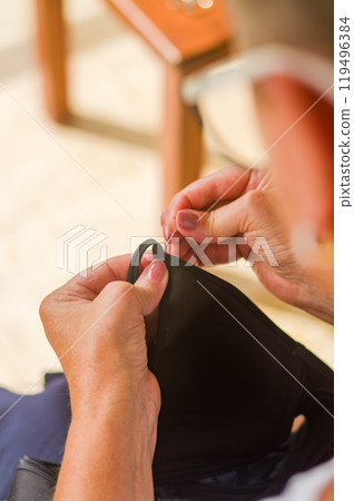 The hands of a senior woman who uses needle and thread to repair a black garment. High quality photo The hands of a senior woman who uses needle and thread to repair a black garment. High quality photo 119496384