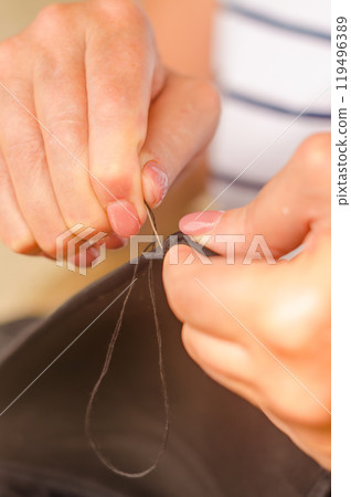 hands of a senior woman who uses needle and thread to repair a black garment. . High quality photo 119496389