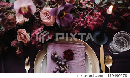 Dinner table setting in the warm glow of candlelight, tablescape featuring floral centerpiece, elegant burgundy glassware, and luxurious gold cutlery, all contributing to a sophisticated dining 119496678