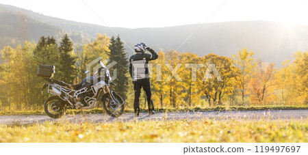 Motorcyclist watching the countryside on scenic autumn forest trail. 119497697