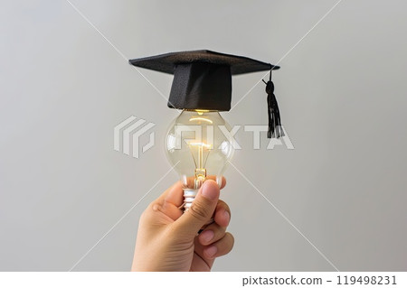 An individual is holding a light bulb that is wearing a graduation cap 119498231