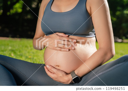 Pregnant fitness model in sportswear doing yoga or Pilates sitting on grass outdoor 119498251