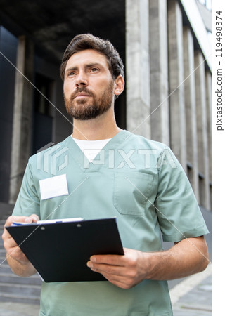 Man doctor wearing uniform filling in medical form standing outdoors of modern clinic Man doctor wearing uniform filling in medical form standing outdoors of modern clinic 119498374