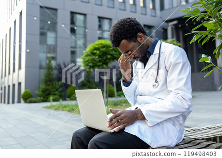 Tired doctor wearing his uniform at hospital using his laptop for online consultation Tired doctor wearing his uniform at hospital using his laptop for online consultation 119498403