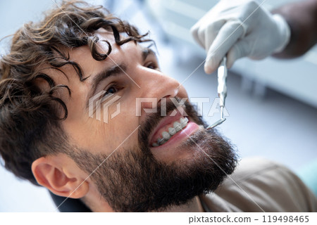 Young man sitting in dentist chair while doctor examining his teeth Young man sitting in dentist chair while doctor examining his teeth 119498465