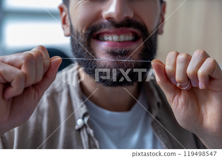 Man holding dental floss following hygiene routine to maintain fresh and healthy teeth and braces Man holding dental floss following hygiene routine to maintain fresh and healthy teeth and braces 119498547